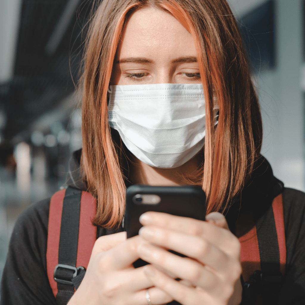 Woman with facemask holding smartphone.